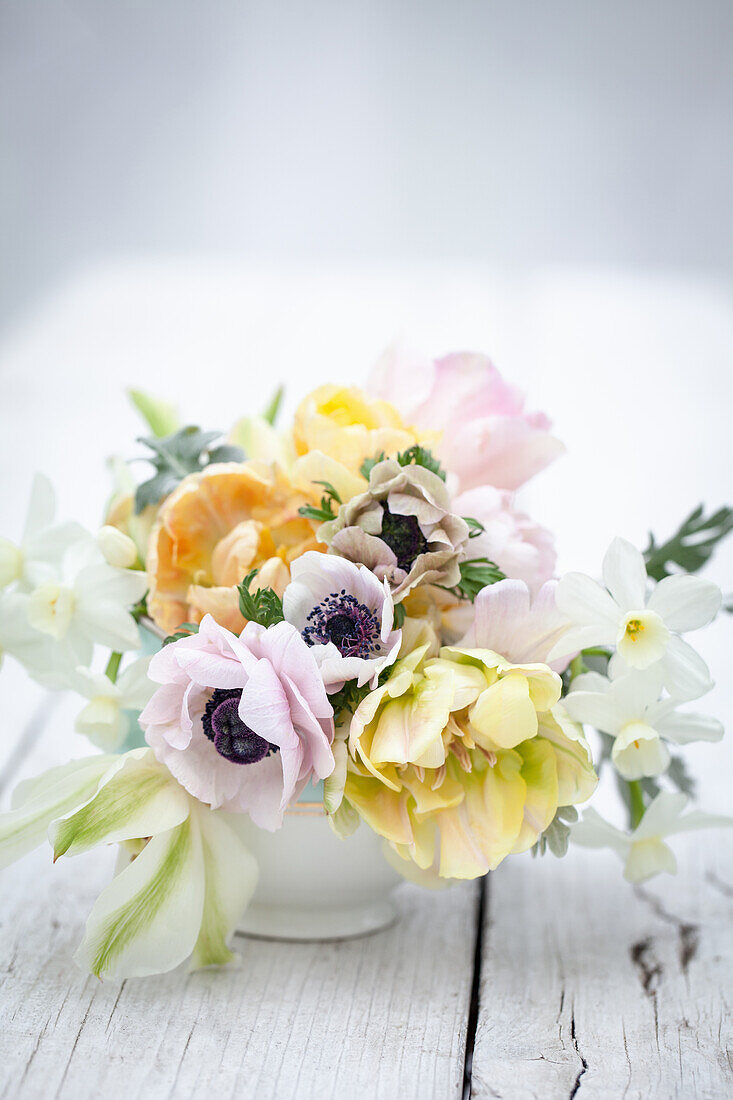 Kleines Frühlingsblumenarrangement mit pastellfarbenen Anemonen, Tulpen und Narzissen