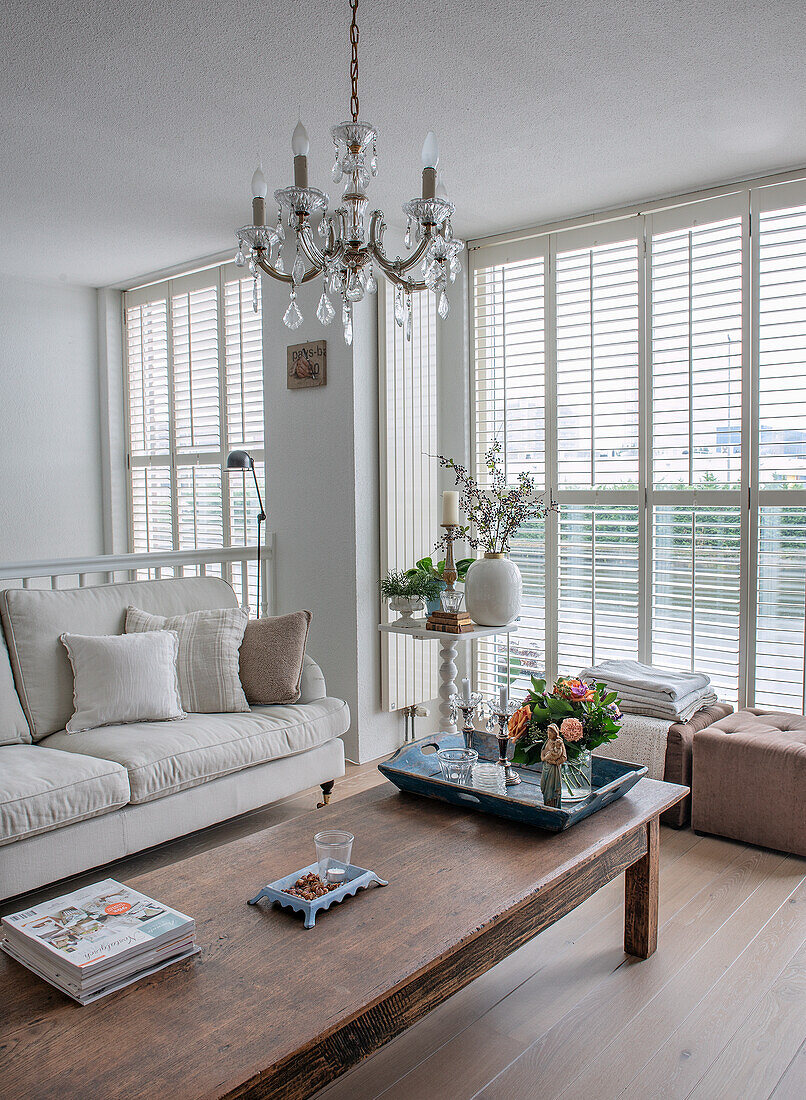 Helles Wohnzimmer mit Holztisch, Kristallleuchter und großen Fensterläden