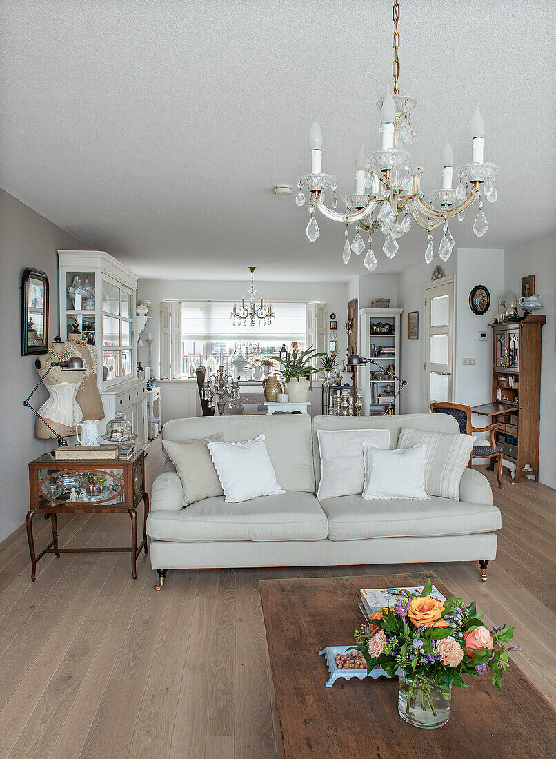 Living room with chandeliers, beige couch and bouquet of flowers on wooden table