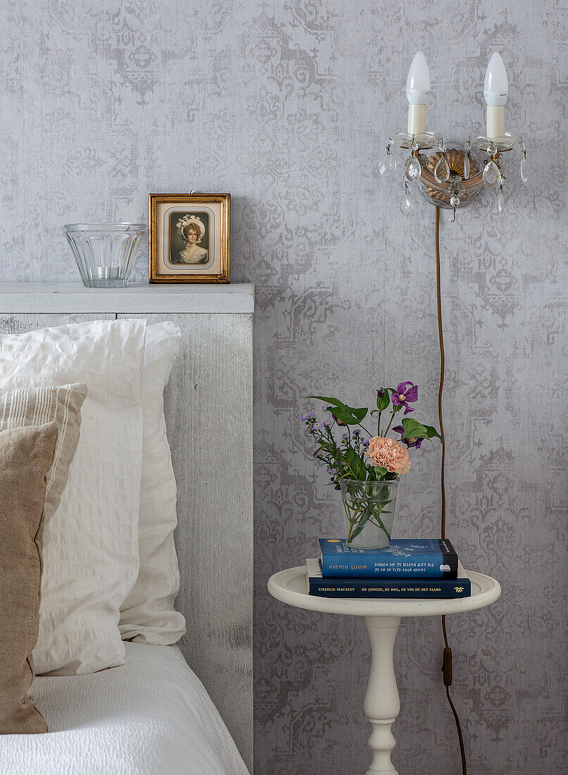 Bedroom with vintage wallpaper, bedside table, wall lamp and bouquet of flowers