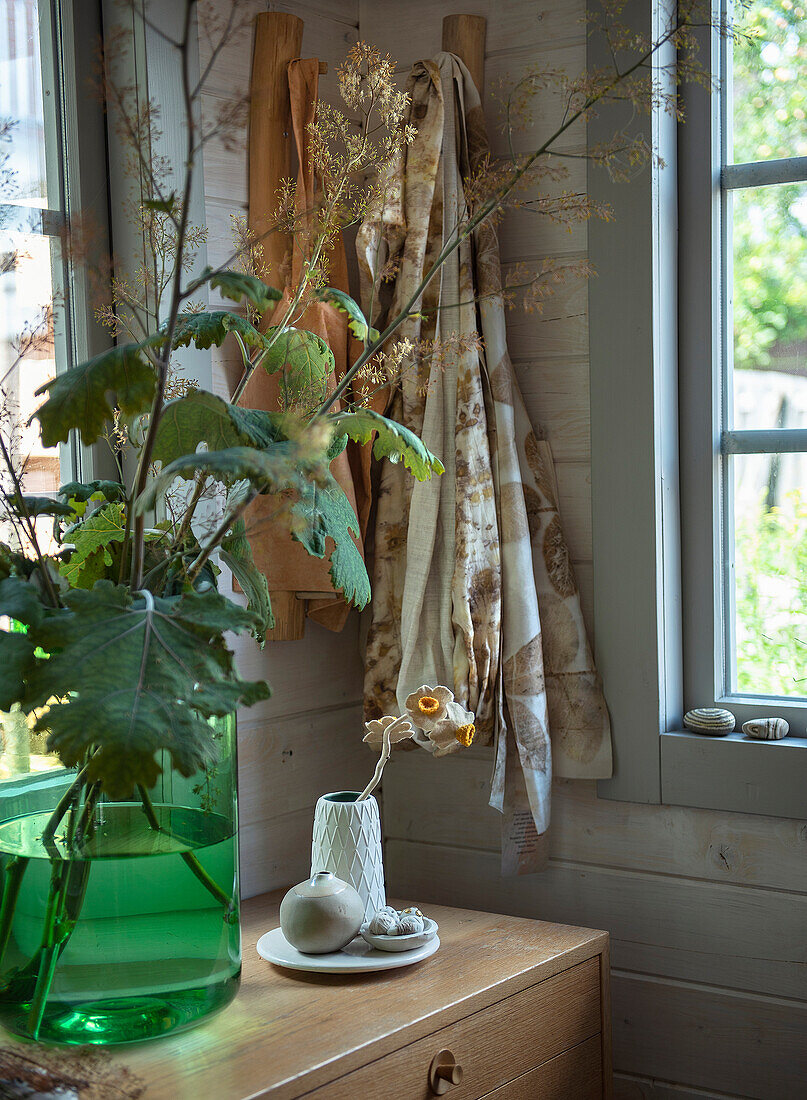 Vase with green leaves on chest of drawers in wooden panelling