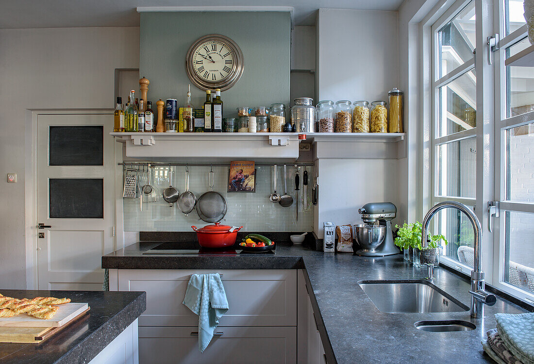 Bright kitchen with large window, clock and open shelf for storage jars and oils