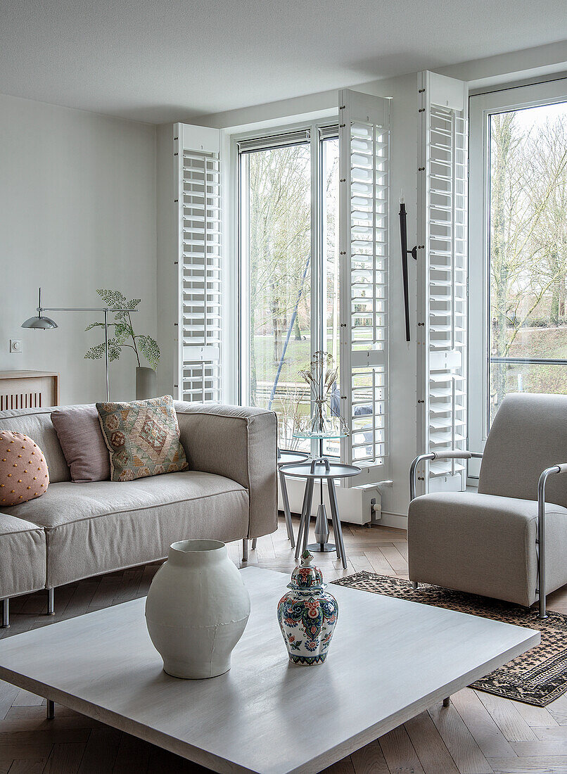 Living room with sofas, mullioned windows and decorative vases on a wooden table