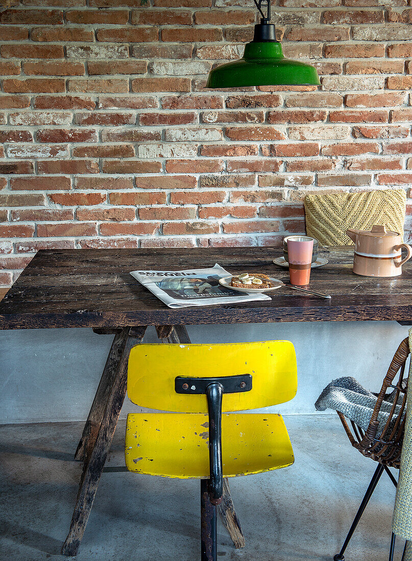 Wooden table with old-fashioned yellow chair in front of a brick wall