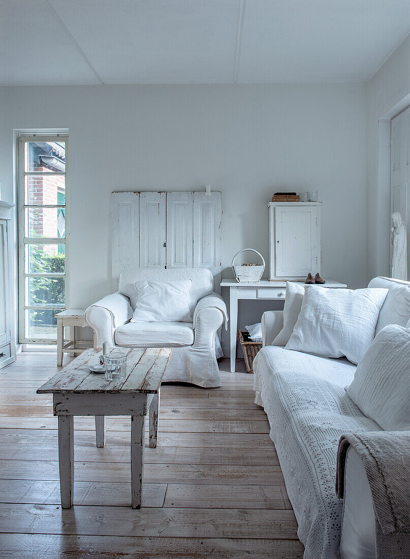 Weißes Wohnzimmer mit Sessel, Sofa und rustikalem Holztisch