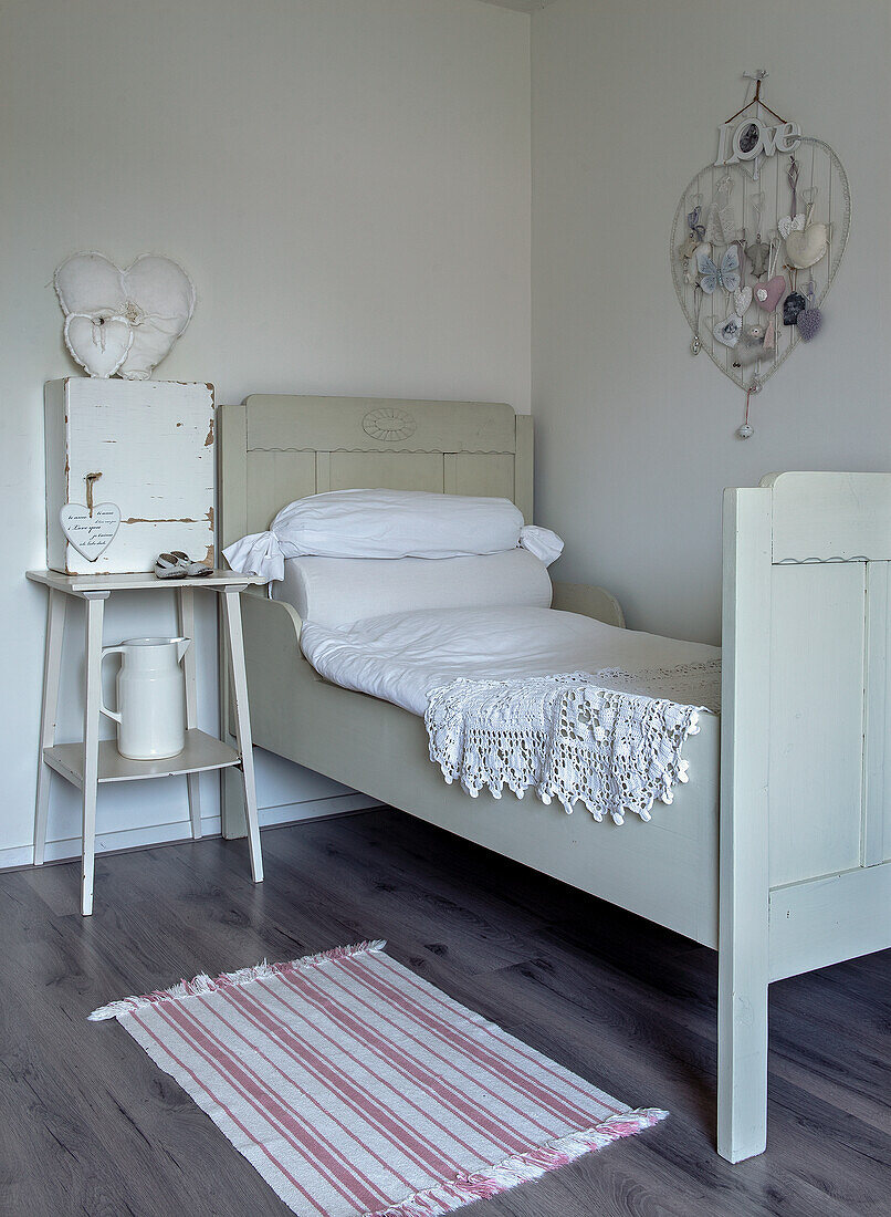 Cot with crocheted blanket, white side table and wall decoration