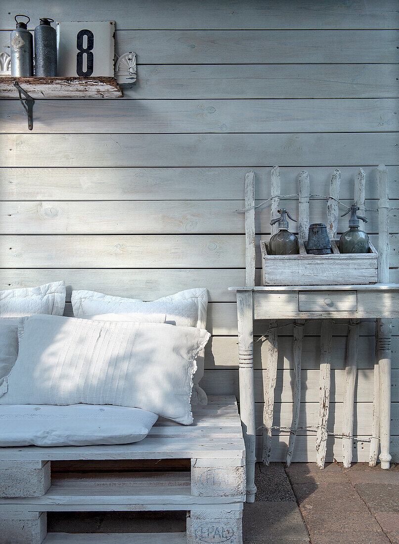 White-painted wooden wall with pallet bench and side table in a shabby chic look