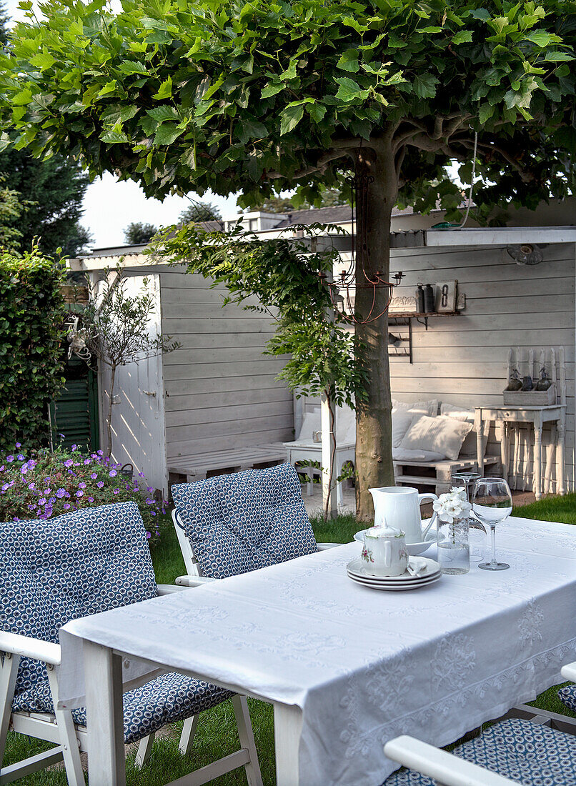 Gedeckter Gartentisch unter Baum, überdachte Terrasse im Hintergrund