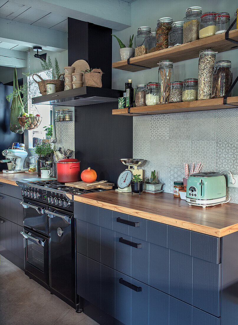 Kitchen with open shelving with storage jars, black cupboards and wooden countertops