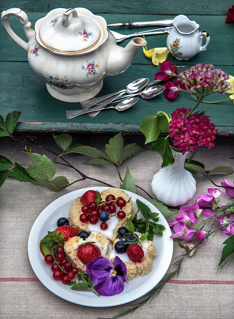 Tea cakes decorated with berries and flowers on a rustic wooden table