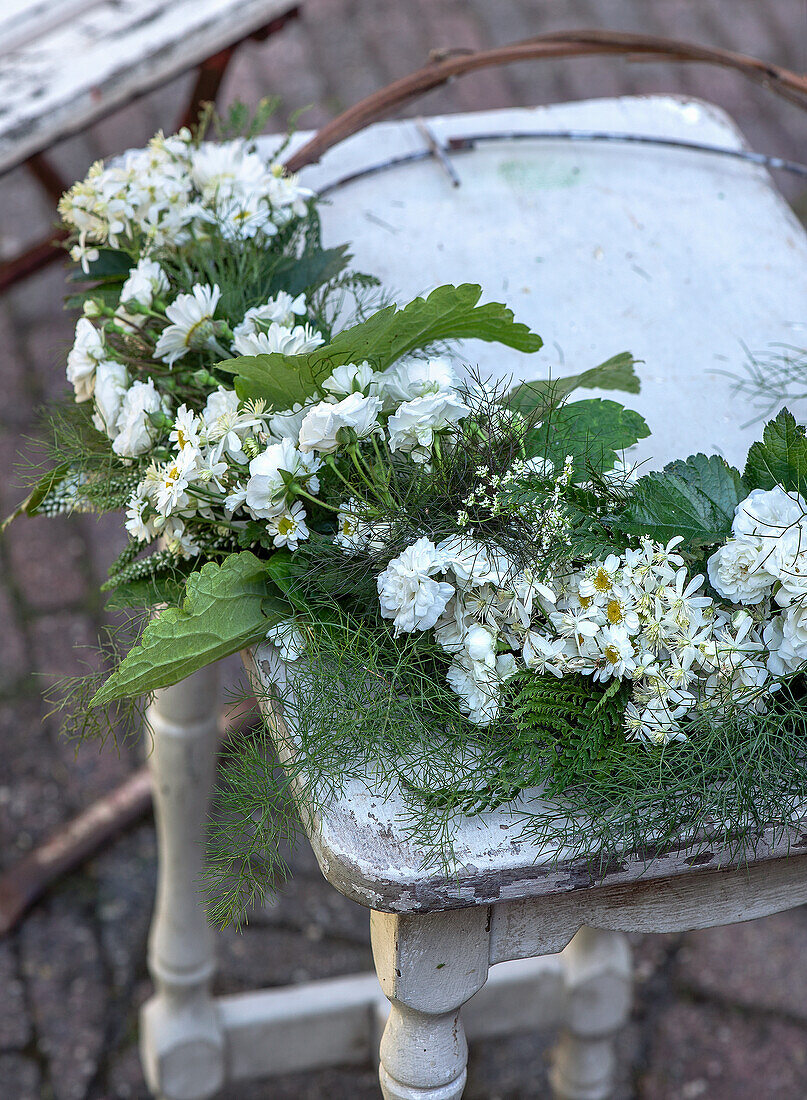 Blumengesteck aus weißen Rosen und Margeriten auf rustikalem Tisch im Garten