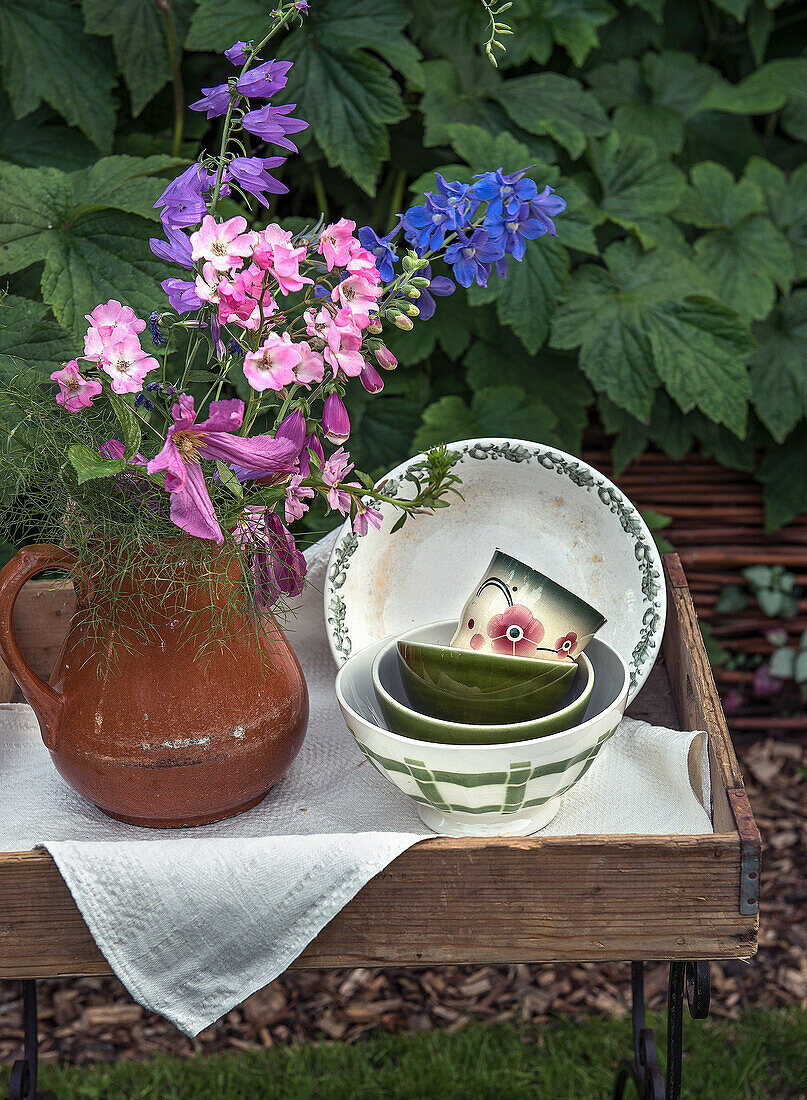 Bouquet of flowers with delphinium in clay jug and ceramic bowls on wooden table