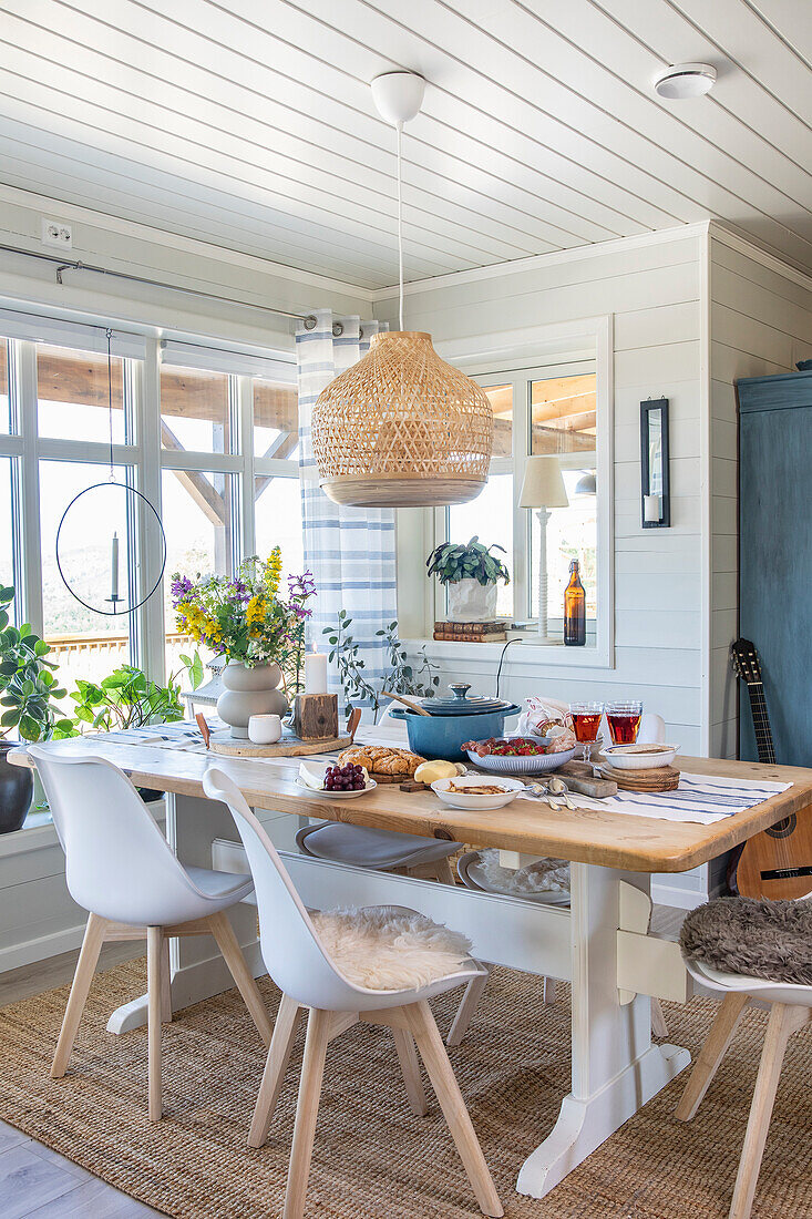 Dining room with richly laid table, white chairs and wicker lamp