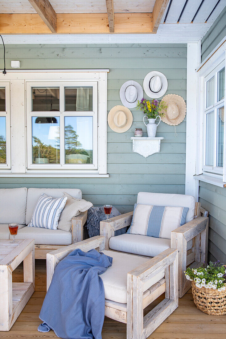 Covered terrace with wooden seating furniture, hats on the wall and floral decorations