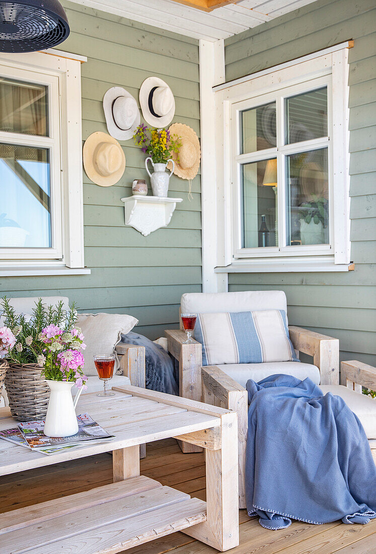 Gemütliche Veranda mit rustikalen Holzmöbeln, salbeigrüner Wand und Sommerhut-Dekoration