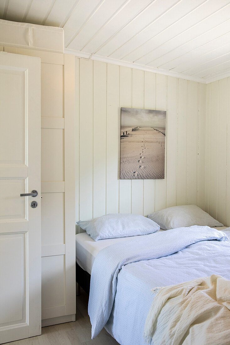 Schlafzimmer mit weißer Holzverkleidung und Strandbild an der Wand