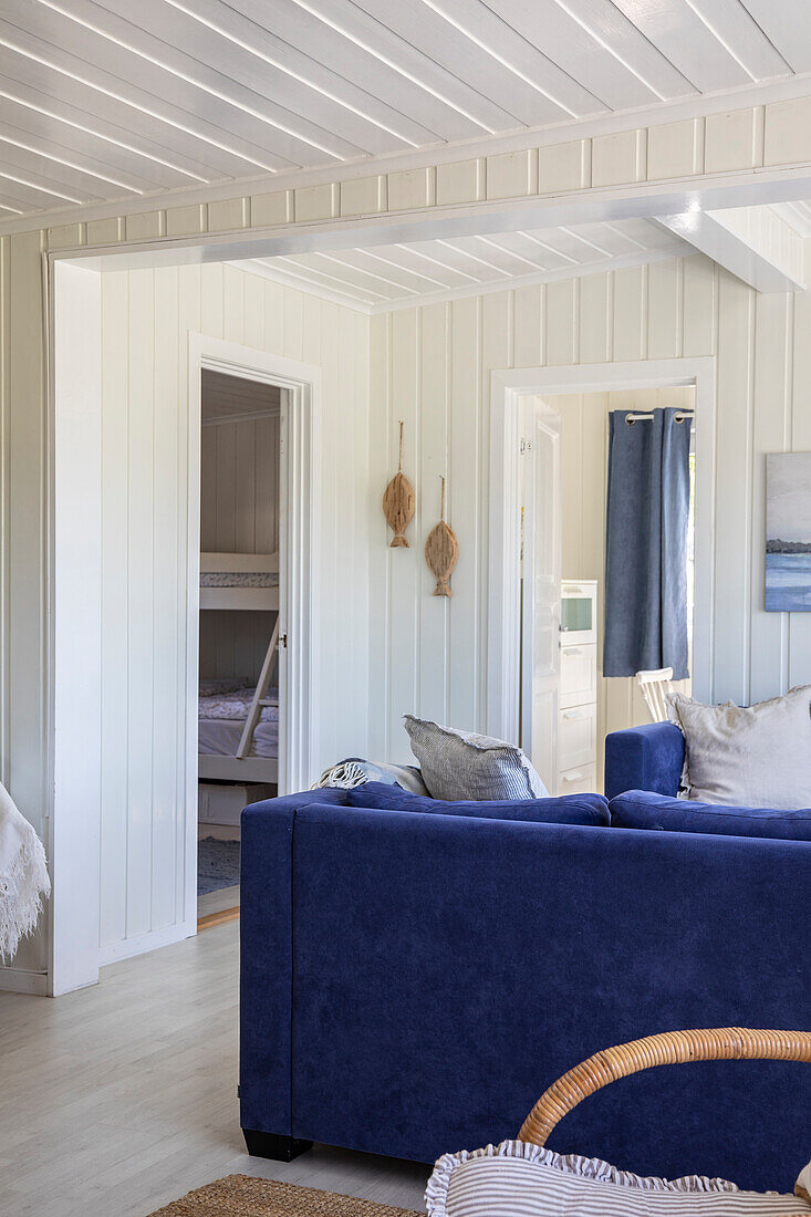 Living room with dark blue sofa, white wood paneling and view of the children's room with bunk bed