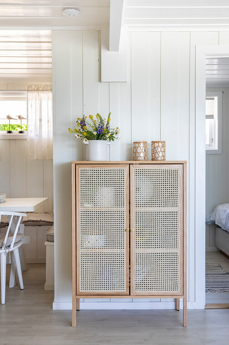 Wickerwork sideboard with flower vase and tea lights in front of white paneling in the hallway