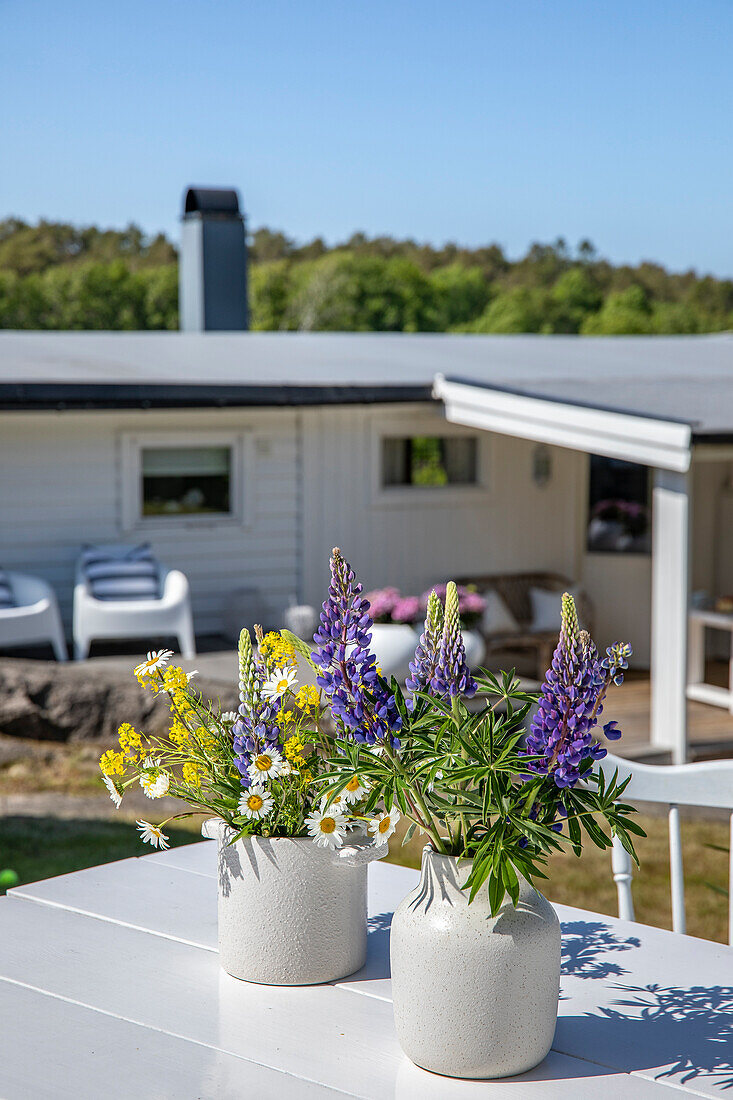 Sommerliche Blumendekoration mit Lupinen und Gänseblümchen auf weißem Terrassentisch