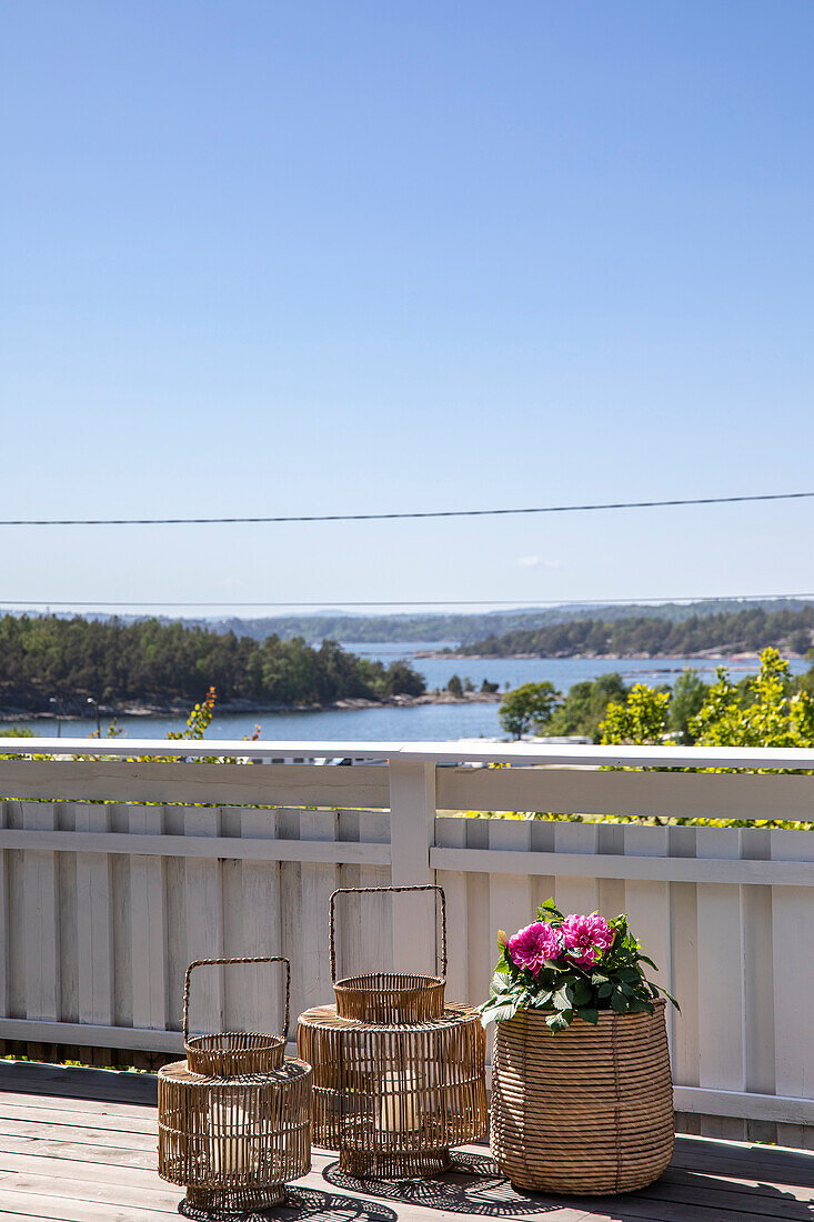 Two woven wicker lanterns and basket with flowers on terrace with sea view