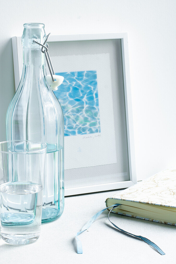 Still life in cool blue-turquoise tones with glass bottle, book and watercolor with water reflections