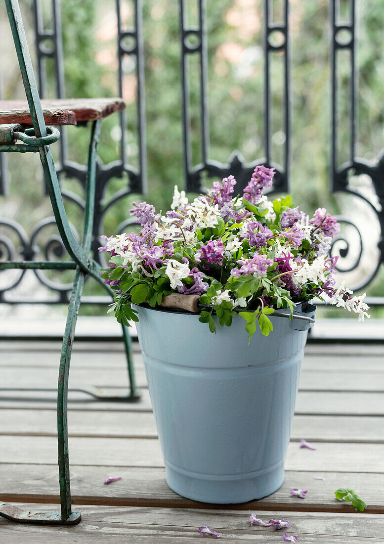 White and purple flowers in blue metal bucket on balcony with wrought iron railing