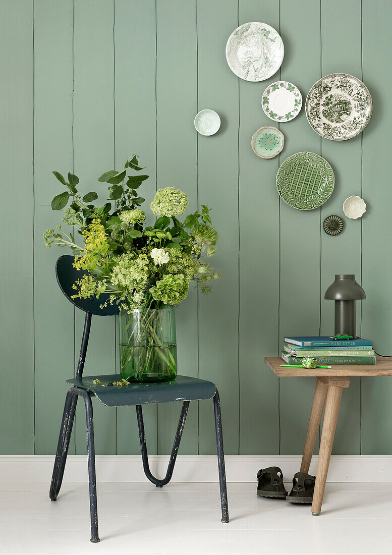 Bouquet of flowers in glass vase on dark green chair in front of green-painted wooden wall