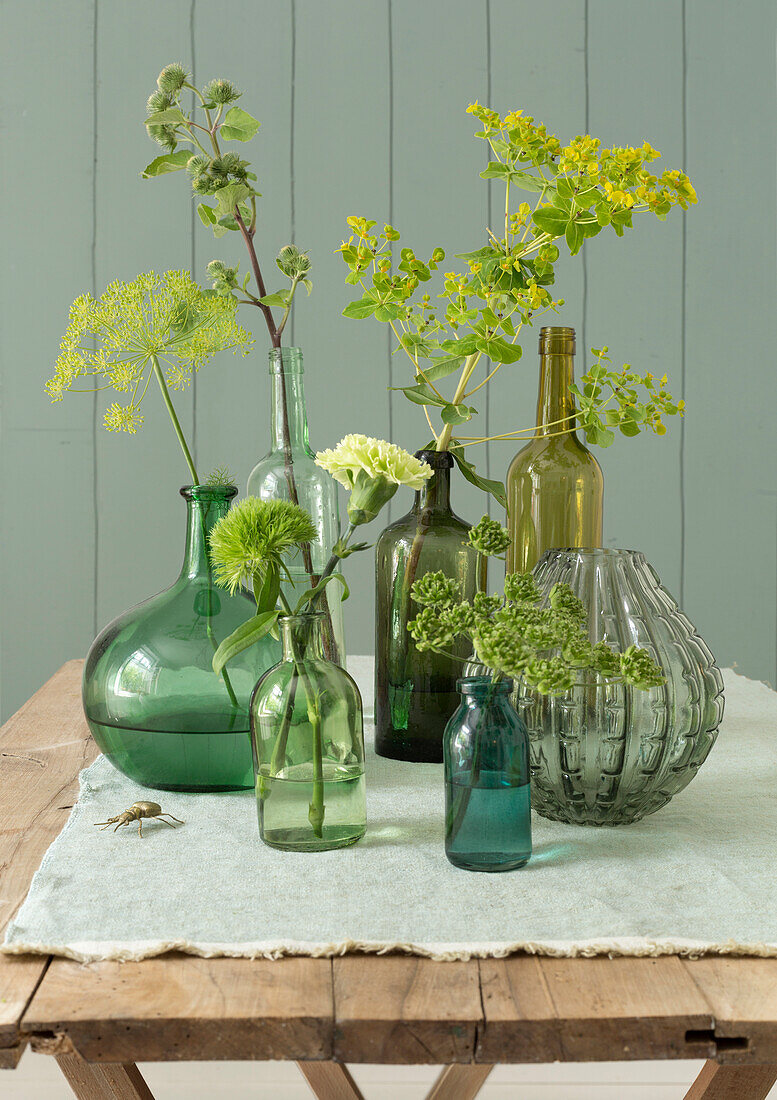 Glasvasen mit grünen und gelben Blumenarrangements auf rustikalem Holztisch