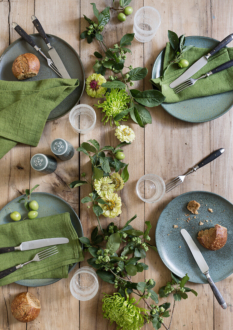 Gedeckter Holztisch mit Geschirr, Servietten und Blumenarrangement in Grüntönen