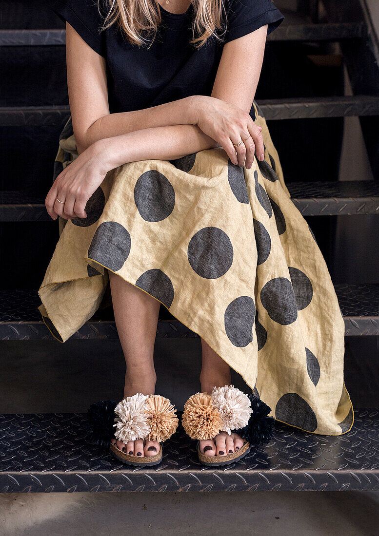 Person mit gepunktetem Rock und Sandalen mit Pompons auf Metalltreppe