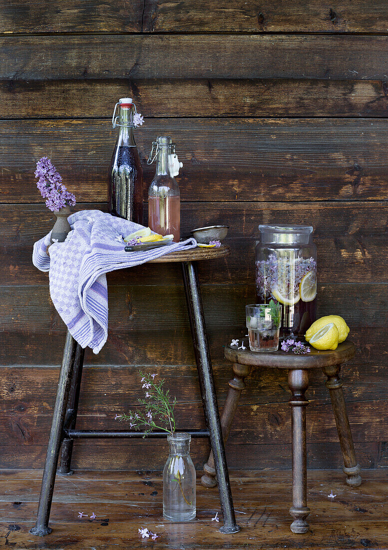 Homemade lavender lemonade in glass jars on a rustic stool and side table in front of wooden panelling