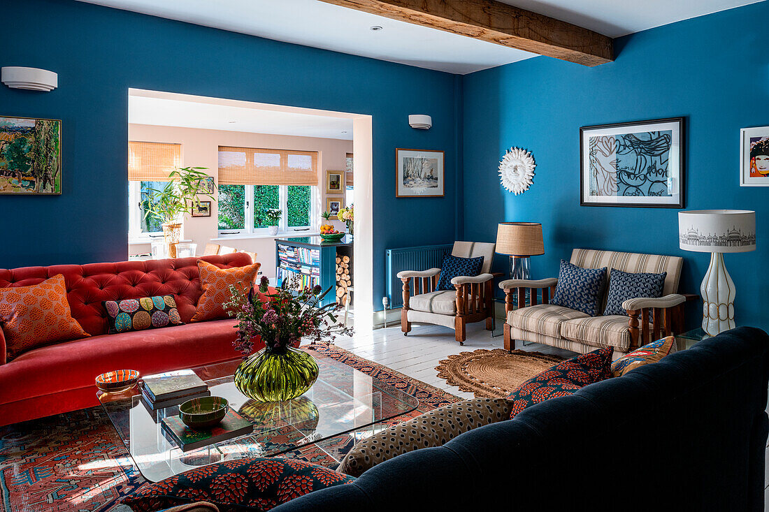 Living room in blue and red tones with wooden beams and glass table