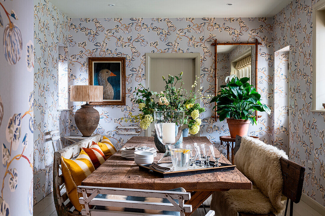 Rustic dining room with wooden table, benches and floral patterned wallpaper