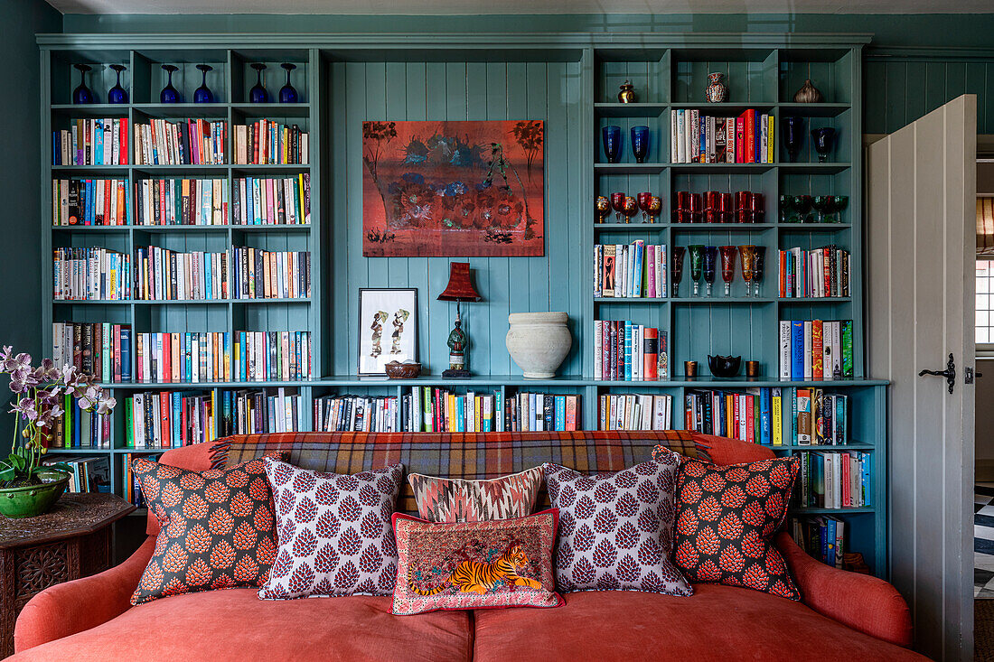 Wohnzimmer mit hellblauer Bücherregalwand, rotem Sofa und gemusterten Kissen