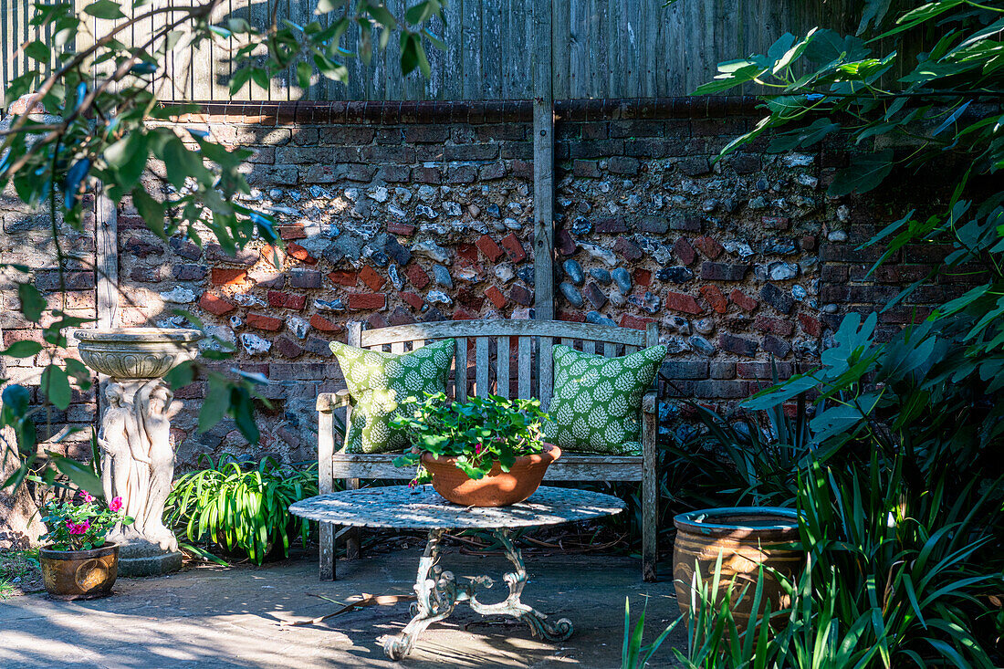 Seating area in the garden with stone table and wooden bench in front of brick wall