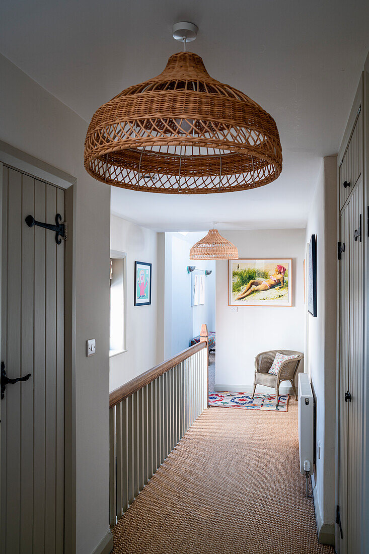 Hallway with wicker lamps and sisal carpet, with armchair and framed art in the background