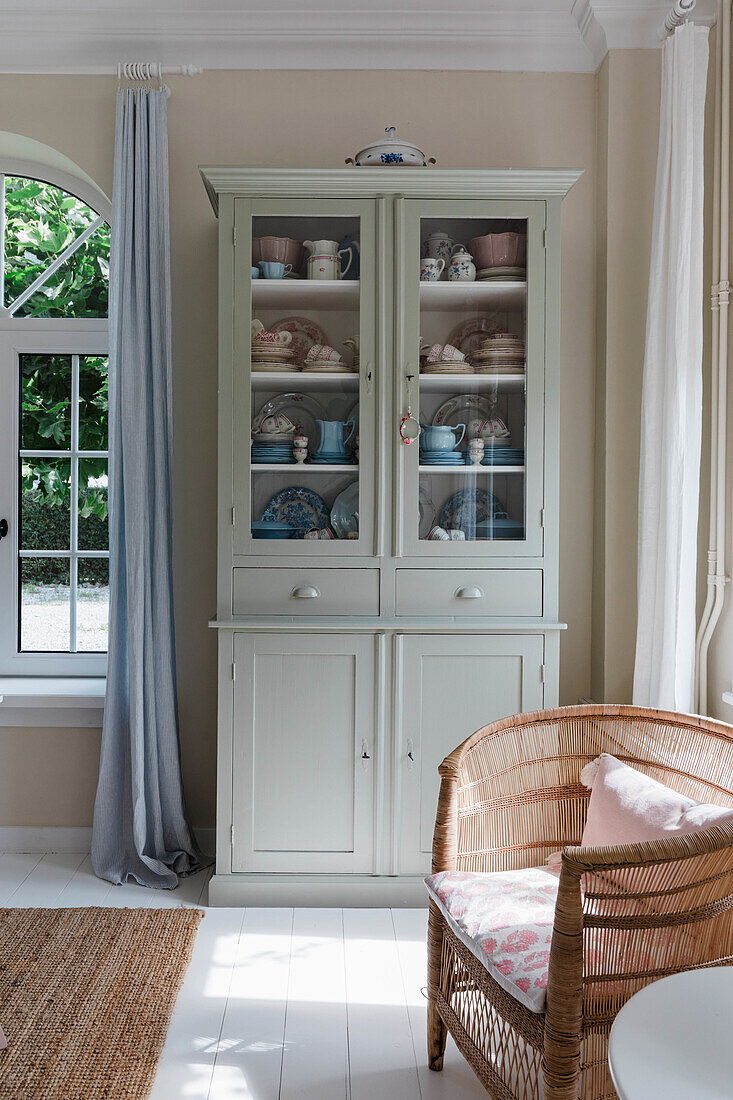 Rattan armchair in front of display cabinet with country-style porcelain