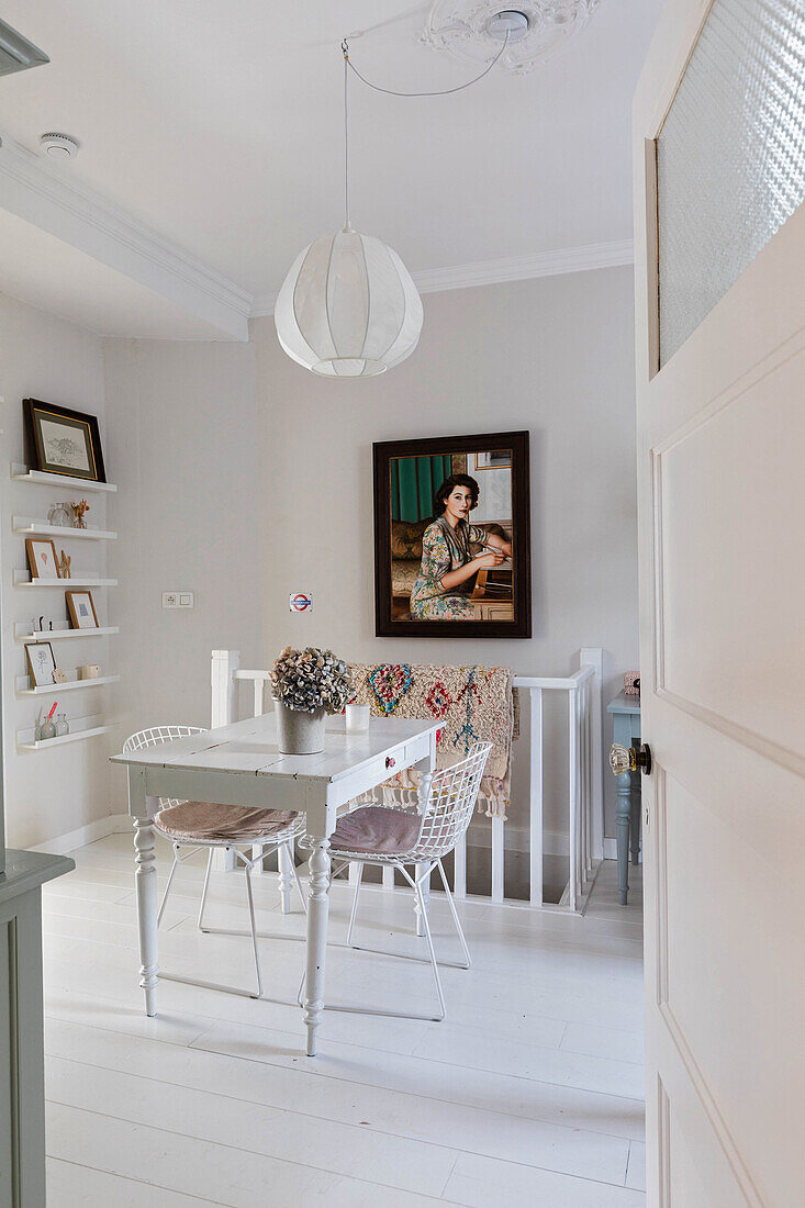 Dining room with white wooden table, metal wicker chairs and picture shelf