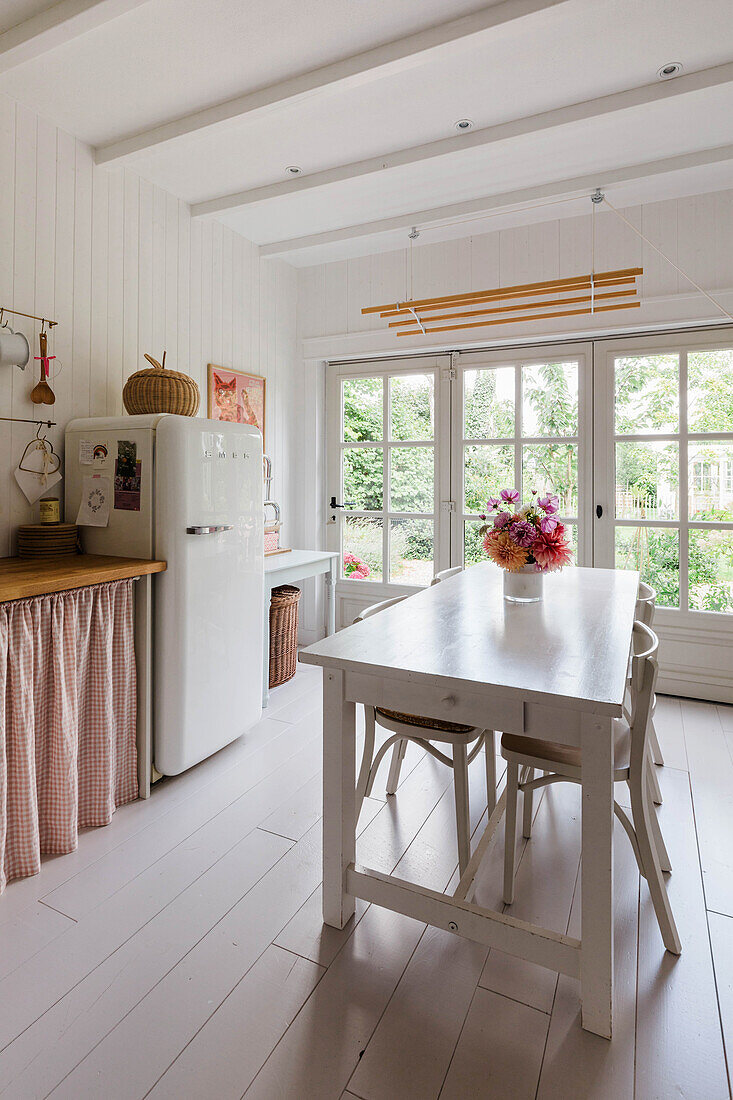 Weiße Landhausküche mit Holztisch, Blumenvase und Retro-Kühlschrank