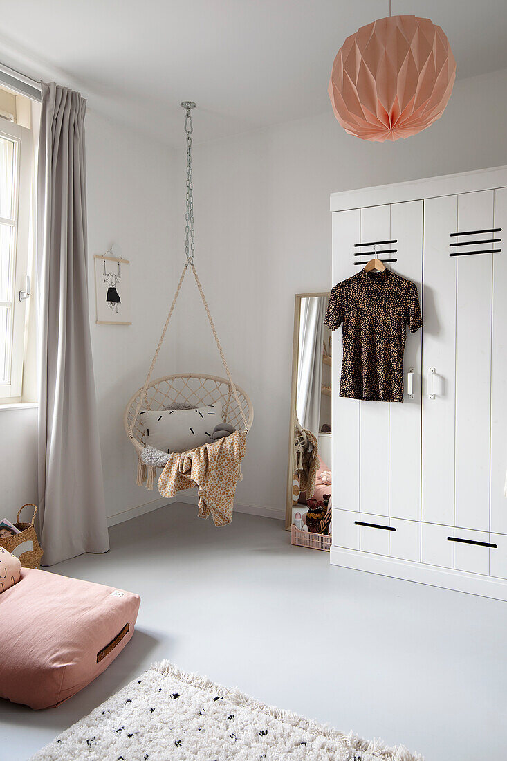 Brightly furnished children's room with hanging chair and wardrobe in white