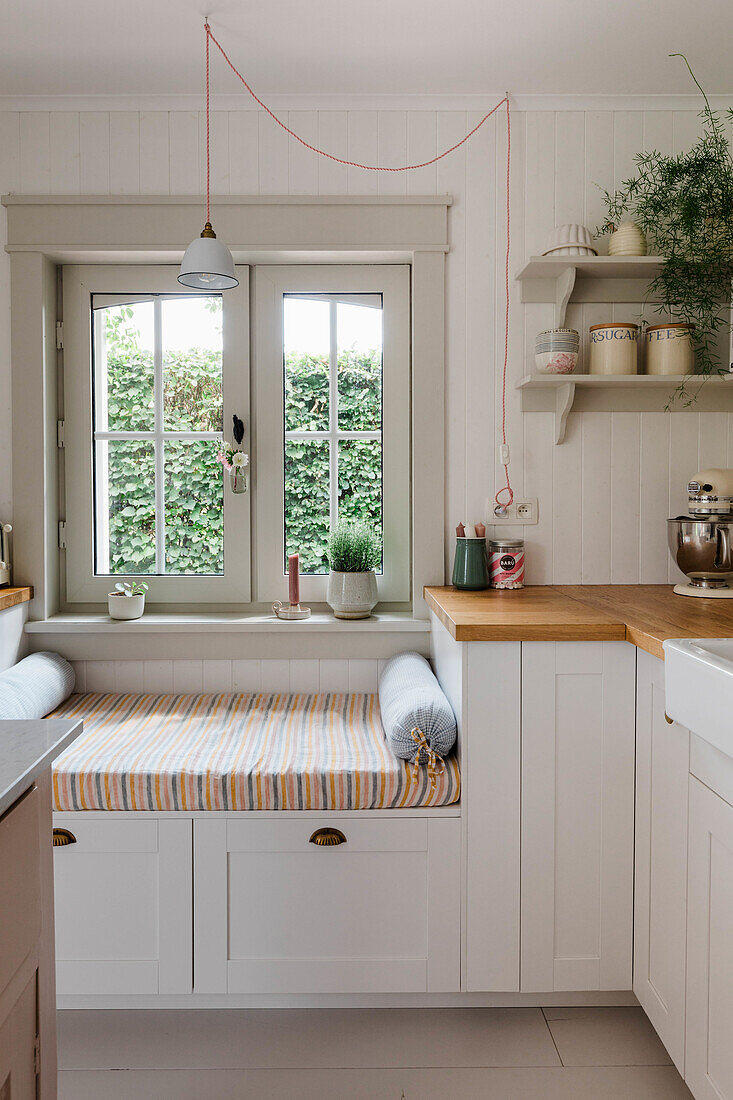 Seating window sill in country kitchen with wooden worktop and open shelf