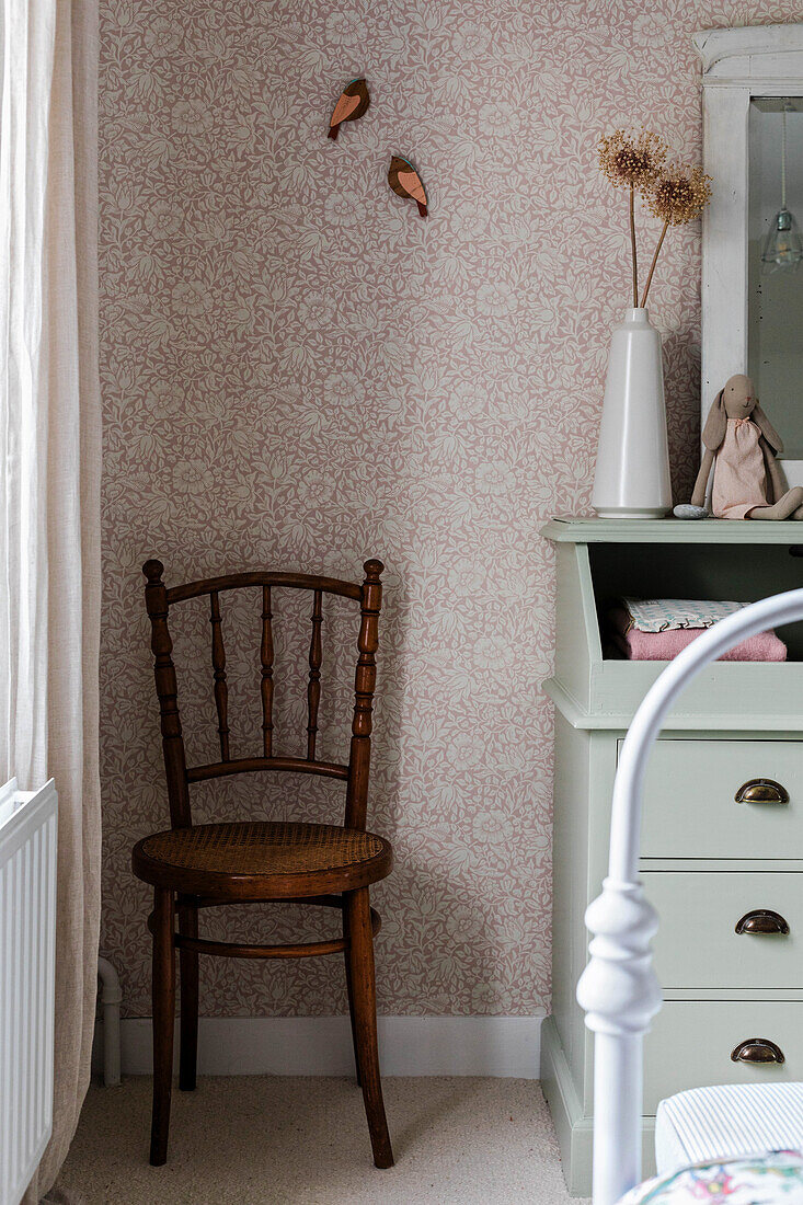 Corner of a children's room with wooden furniture and floral patterned wallpaper