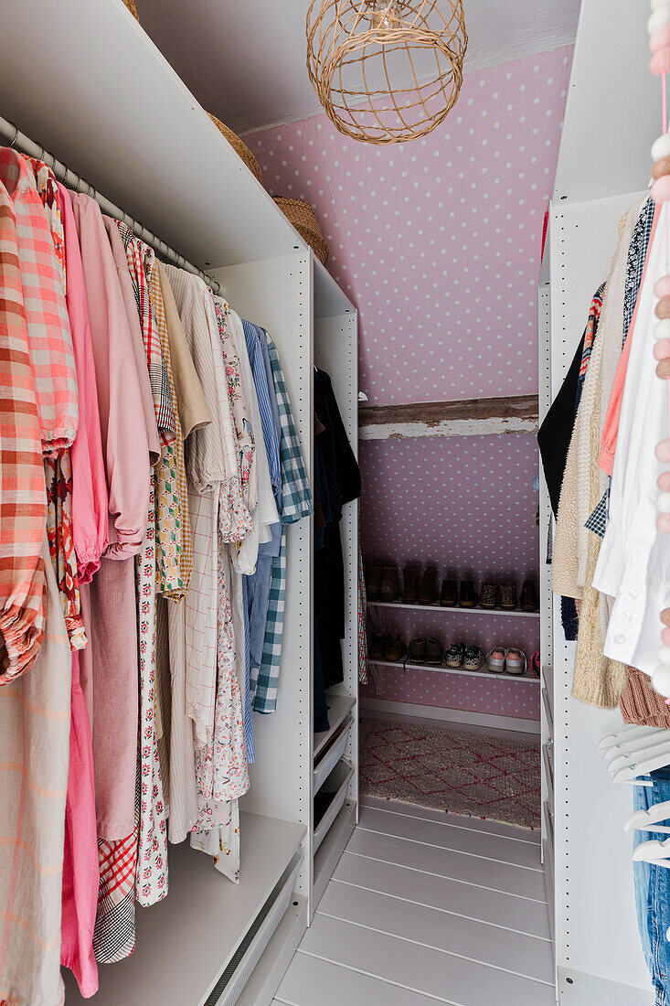 Dressing room with pink dotted wallpaper and clothes in the wardrobe