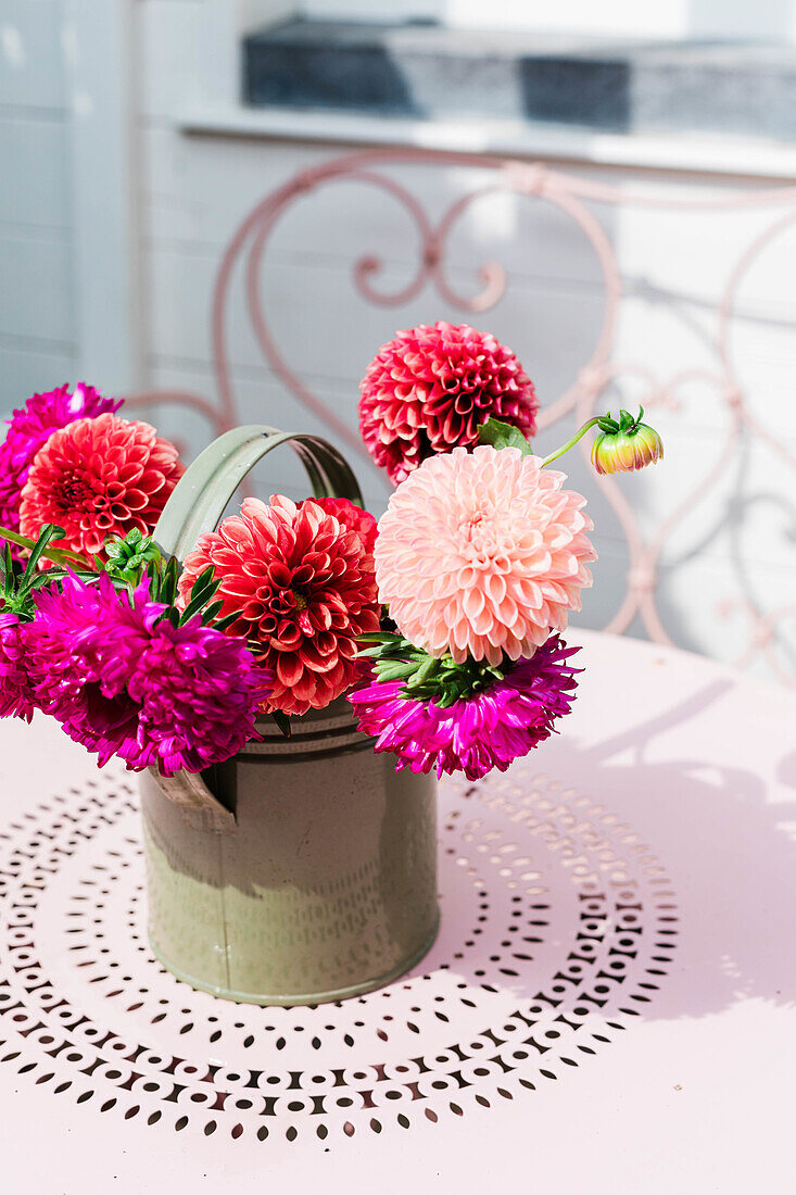 Colourful dahlias (Dahlia) in a green watering can on a stamped metal table