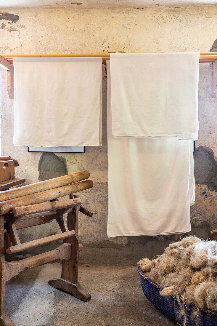 Linen fabrics on wooden poles in rustic room, basket with flax