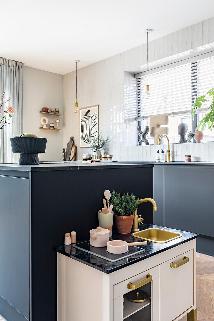 Modern kitchen with black cupboards, white tiled wall and children's kitchen in the foreground