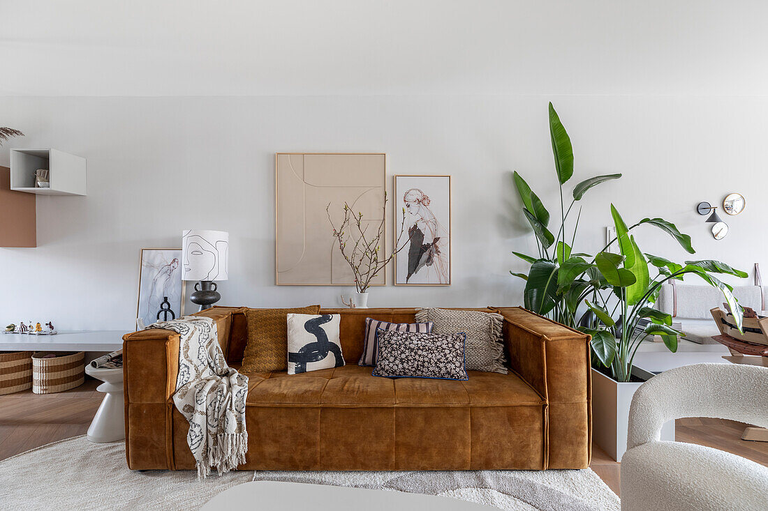 Wohnzimmer mit braunem Verlour-Sofa, Pflanzen und moderner Kunst an der Wand