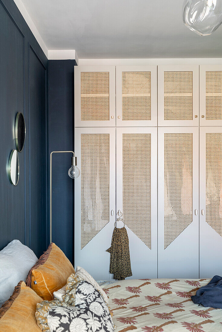 Bedroom with blue-painted wall and wardrobes with rattan fronts