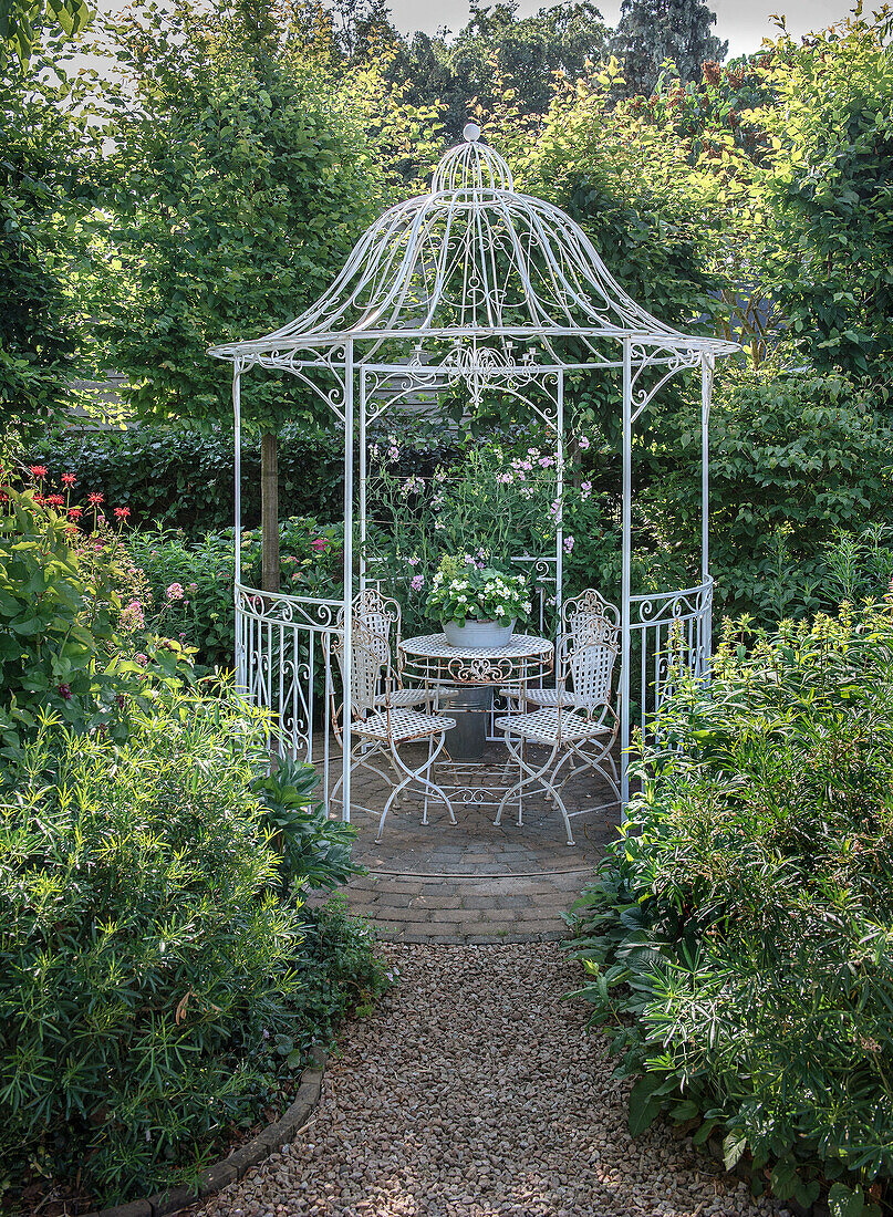 White arbour with metal table and chairs in a lush garden