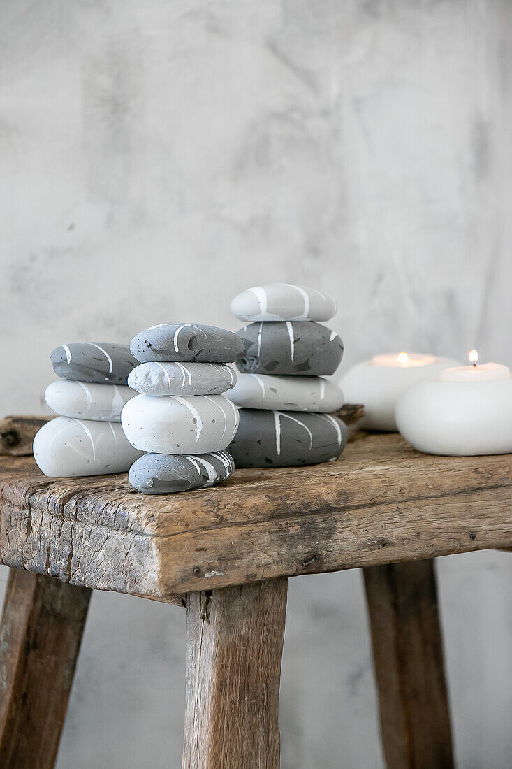 Stacked, painted stones in shades of grey and white with burning candles on a rustic wooden stool